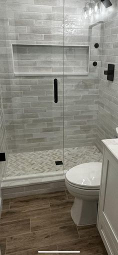 a bathroom with a walk in shower next to a white toilet and wooden flooring