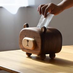 a wooden bear tissue dispenser on top of a table with someone's hand