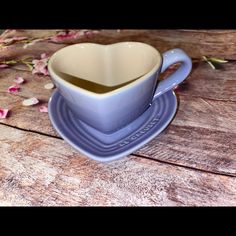 a heart shaped cup and saucer on a wooden table with pink flowers in the background