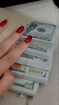 a woman's hand with red nail polish holding stacks of money