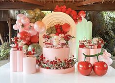 a table topped with lots of pink and red cakes covered in balloons next to tomatoes