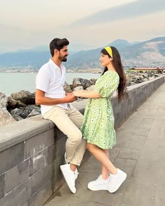 a man and woman sitting on a wall near the water