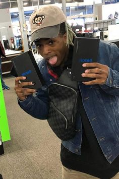 a man with his tongue hanging out holding two black boxes in one hand and a hat on the other