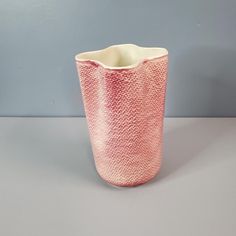 a pink vase sitting on top of a white table next to a gray wall and floor