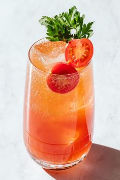 a close up of a drink in a glass with a tomato on the rim and garnish