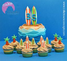 cupcakes with frosting and surfboards are arranged in front of a cake