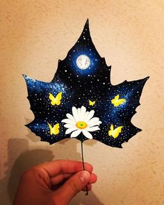 a hand holding up a paper leaf with flowers on it and the moon in the background