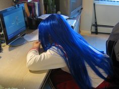 a woman with blue hair sitting at a desk in front of a computer