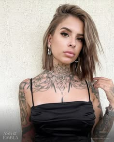 a woman with tattoos on her chest posing for the camera while wearing a black dress