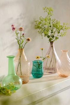 several vases with flowers in them sitting on a shelf next to a white wall