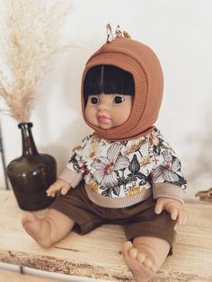 a doll sitting on top of a wooden table next to a vase and a plant