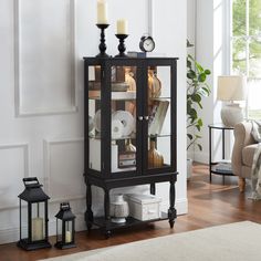 a glass cabinet with candles and other items on it in a living room next to a couch