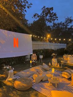 an outdoor movie is set up in the evening with lights on and furniture laid out