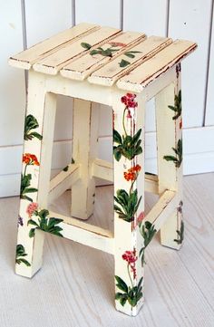 a small wooden stool with flowers painted on the sides and bottom, sitting against a white wall