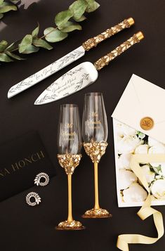 two champagne flutes with gold rims are next to an envelope and some other items