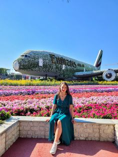 a woman sitting on a bench in front of a flower garden with an airplane sculpture behind her