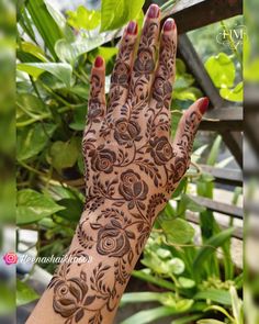 a woman's hand with henna on it and green plants in the background