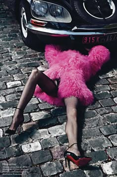 a woman laying on the ground next to a pink teddy bear in front of a car