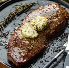 a steak with butter and herbs on it is sitting on a plate next to a knife