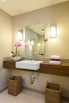 a bathroom sink sitting under a mirror next to a basket filled with flowers and towels