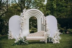 a couch sitting in the middle of a lush green field next to a white arch