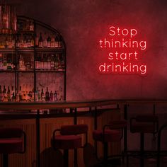 a red neon sign that says stop thinking start drinking in front of a bar filled with liquor bottles