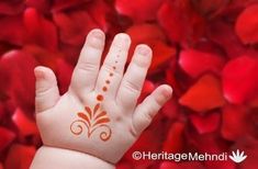 a baby's hand with a hendi on it and red petals in the background