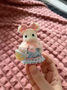 a hand holding a small toy bear with a pink bow on it's head