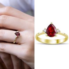 a woman's hand holding a ring with a pear shaped red stone in it