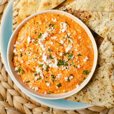 a bowl of hummus and tortilla chips on a blue plate with white cheese