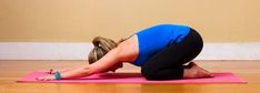 a woman in blue shirt doing yoga on pink mat