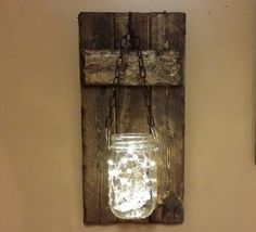 a mason jar hanging on a wall with chains attached to it and a light inside