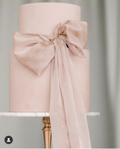 a pink wedding cake with a large bow on it's top and gold legs