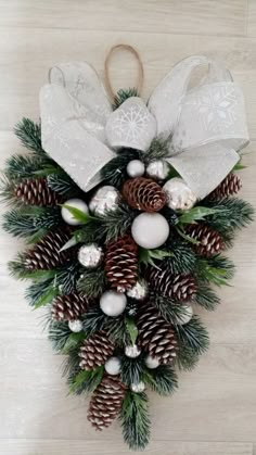 a christmas wreath with pine cones and white balls hanging on a wall in front of a wooden floor