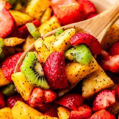 a wooden spoon filled with fruit salad and topped with kiwis, strawberries, oranges, and pineapple