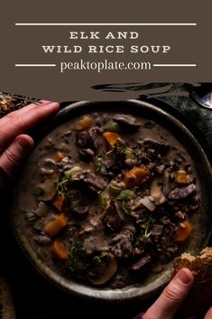 two hands holding a bowl of beef and wild rice soup with bread on the side