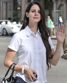 a woman is walking down the street with her hand up in the air while wearing a white shirt and jeans