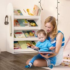 a woman sitting on the floor reading to a child in front of a book shelf