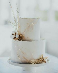 two tiered wedding cake decorated with dried flowers and gold leaf accents on a white table cloth