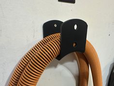 two orange hoses are connected to a black hook on the wall next to a white wall