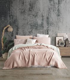 a bed with pink comforter and pillows in front of a gray wall that has peeling paint on it