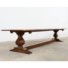 an old wooden table sitting on top of a cement floor next to a white wall