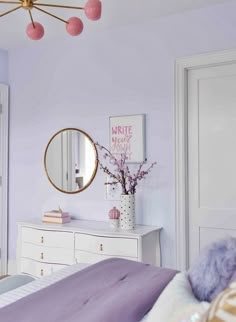 a bedroom with purple walls and white dressers in the corner, along with a round mirror on the wall