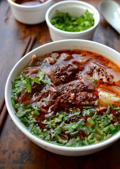 a bowl filled with meat and vegetables on top of a wooden table next to other bowls