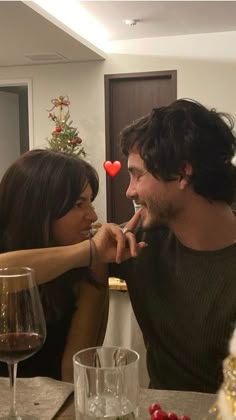 two people sitting at a table with wine glasses in front of them and one person sticking out his tongue