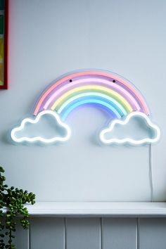 a rainbow shaped neon sign sitting on top of a white shelf next to a potted plant