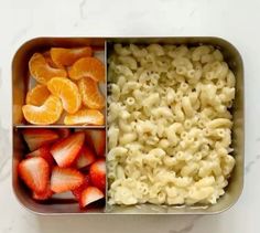 an open lunch box with macaroni, oranges and strawberries