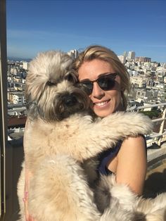 a woman holding a dog in her arms on top of a building overlooking the city