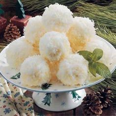 a plate filled with snowball cookies on top of a table next to pine cones