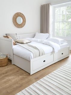 a white bed sitting in a bedroom on top of a hard wood floor next to a window